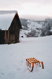 Snow on field against clear sky with wood sledge in front of a cabin during winter