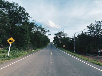 Road sign by trees against sky