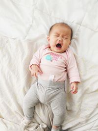 Directly above shot of baby girl yawning while lying on bed