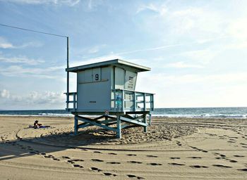 Footprints on sand around lifeguard hut at beach against sky