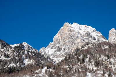 Low angle view of snowcapped mountains against clear blue sky