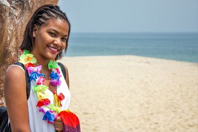 Portrait of smiling young woman with colorful artificial flowers at sandy beach