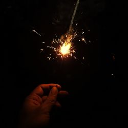 Cropped image of hand holding illuminated fire crackers at night