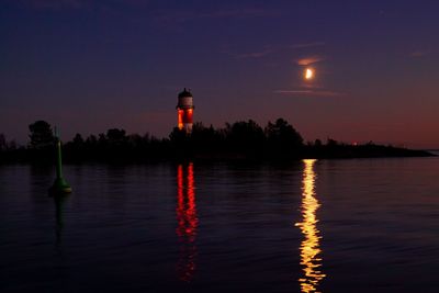 Lighthouse by sea against sky at night