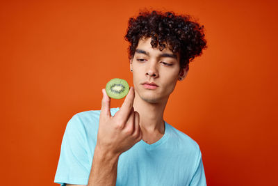 Man looking at kiwi slice against orange background