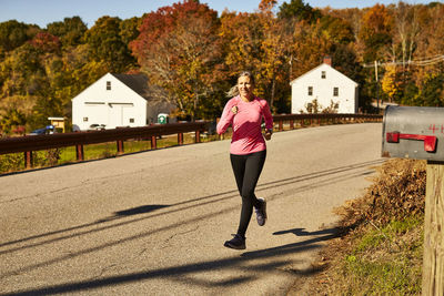 A woman runs down a country road on a autumn day.