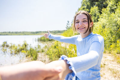 Portrait of young woman with arms raised standing against sky