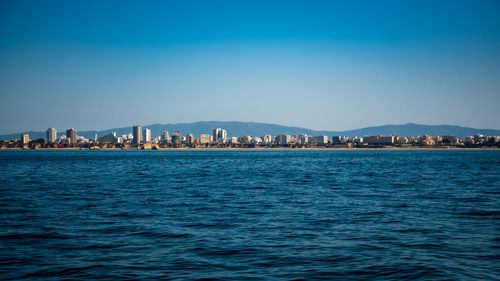 Sea by city against blue sky