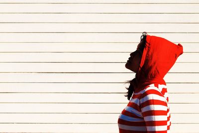 Side view of woman wearing hooded shirt against wall