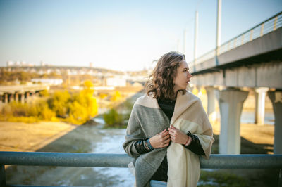 Young woman looking away while standing on bridge against sky