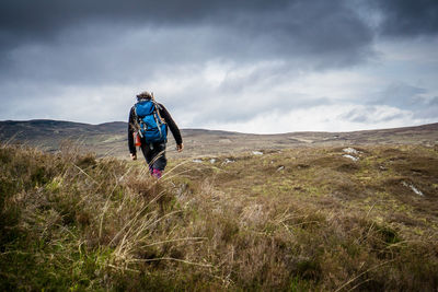 Rear view of man walking on mountain against cloudy sky