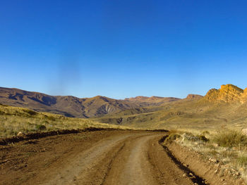 Dirt road leading towards mountains against clear blue sky