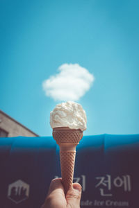 Hand holding ice cream cone against blue sky