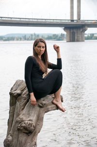 Portrait of smiling young woman sitting against water