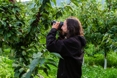 Full length of senior man photographing while standing on plants