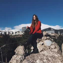 Woman sitting on rock against blue sky