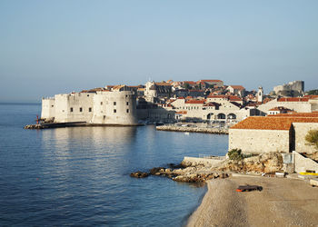 Buildings by sea against clear sky