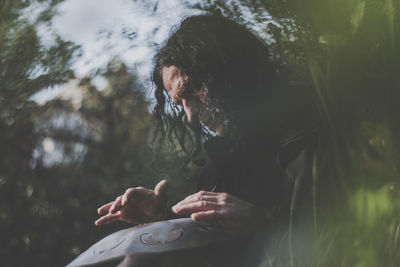 Low angle view of mature man playing music instrument while sitting amidst plants