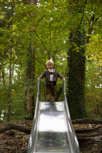 Portrait of cute boy standing on slide against trees
