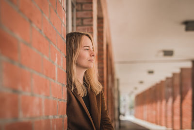 Young woman looking away while standing by brick wall