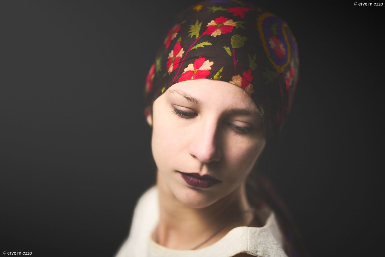 portrait, one person, headshot, adult, women, studio shot, cap, indoors, young adult, turban, headscarf, black background, clothing, hat, human head, headgear, close-up, front view, human face, bandana, female, make-up, looking, copy space, fashion, lipstick, eyes closed, emotion, serious