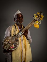 Smiling mature man holding musical instrument against gray background