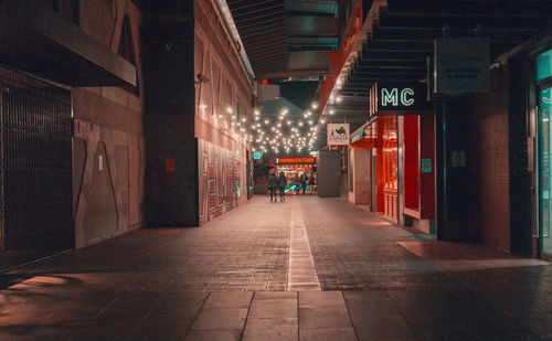 Illuminated footpath amidst buildings in city at night