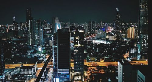 Illuminated modern buildings in city against sky at night