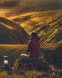 Rear view of woman sitting on rock at sunset