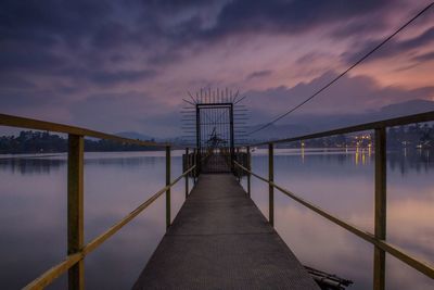 Diminishing perspective of pier over lake against cloudy sky during sunset