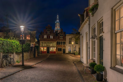 Illuminated street amidst buildings against sky at night