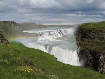 Scenic view of waterfall against cloudy sky