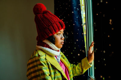 Cute women's winter fashion knitted hat with open curtains looking down the window. red hat.