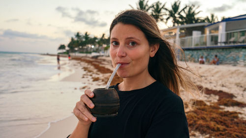 Latina girl drinking argentinian traditional drink called mate in the beach