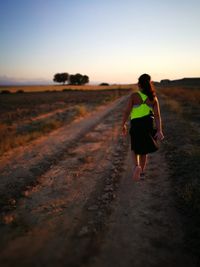 Rear view of woman walking on road against sky during sunset