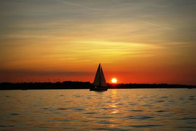 Boat sailing in river against orange sky during sunset