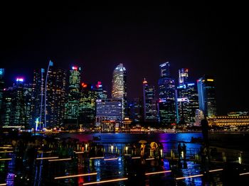 Illuminated buildings by river against sky in city at night