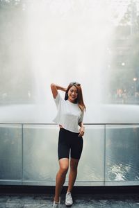 Portrait of smiling woman standing against fountain in city