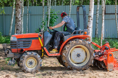 A man on a mini-excavator levels a piece of land, loosens the soil.