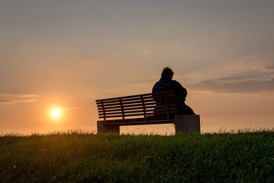 Rear view of silhouette man sitting on field against sky at sunset