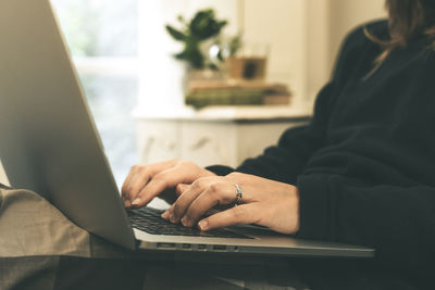 Close up view of girl hands typing on laptop keyboard, sitting on the sofa woman works with computer