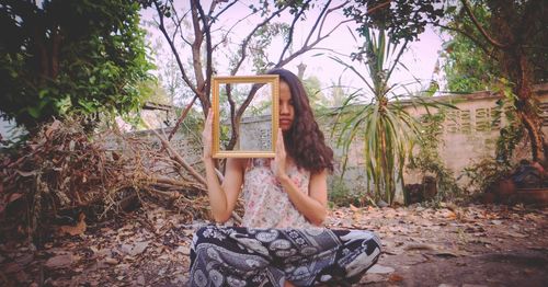 Woman holding picture frame while sitting in messy backyard