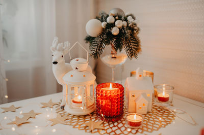 Burning white and red candles, a candlestick of lantern form on napkin, figurinemoose, garlands