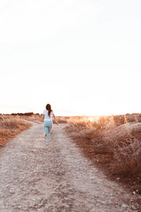 Rear view of woman walking on road against clear sky