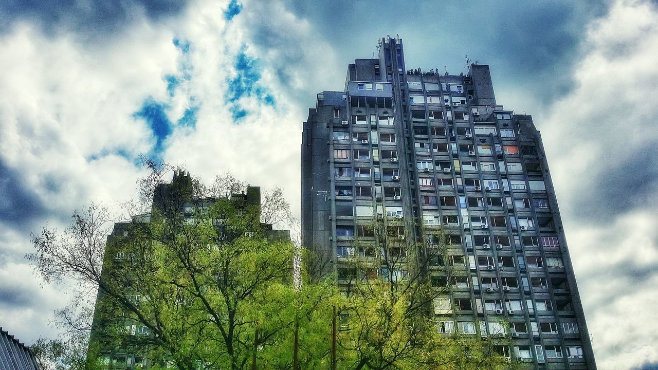 low angle view, building exterior, sky, architecture, built structure, cloud - sky, tree, cloudy, tall - high, growth, cloud, tower, city, modern, day, building, tall, outdoors, green color, no people