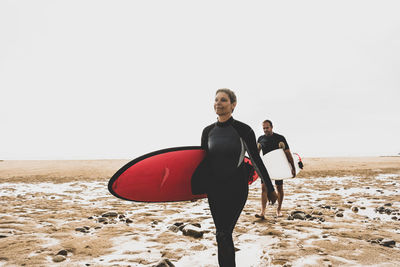 France, bretagne, crozon peninsula, couple walking on beach carrying surfboards