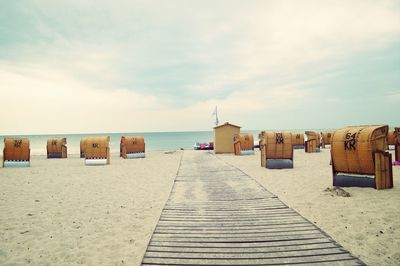 Boardwalk and hooded chair at beach against cloudy sky