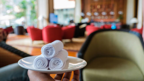 Close-up of human hand holding rolled white towels in plate at restaurant