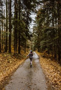 Rear view of girl running on road amidst trees in forest