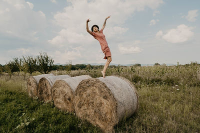 Full length of woman dancing on hay bale against sky